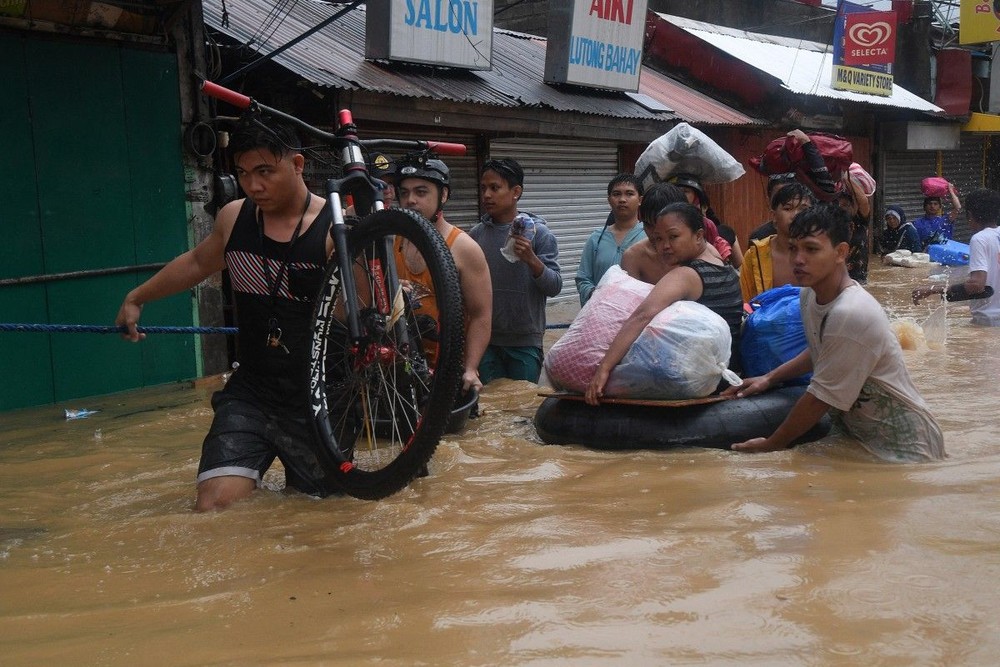 街道被水淹没，人们涉水转移物资。（图：AFP）