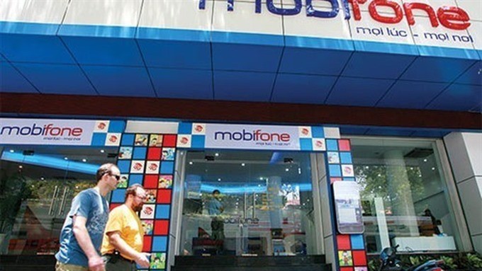 Two foreigners walk pass a customer centre of Mobifone, a State-owned enterprise (SOE) which was under equitisation process. Transparency in privatising SOEs must be enhanced to attract foreign strategic investment. (Photo: vneconomy.vn)