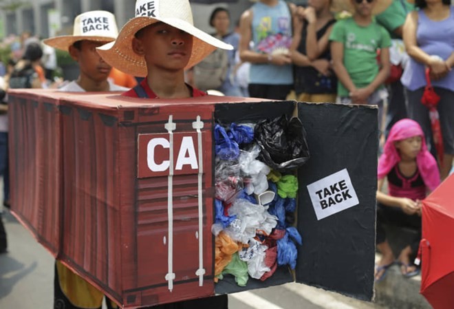 Filipino environmental activists wear a mock container vans filled with garbage to symbolize the 50 containers of waste that were shipped from Canada to the Philippines two years ago as they hold a protest outside the Canadian Embassy in the financial dis