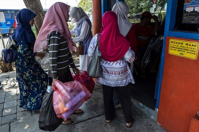 Dozens of people clutching bags full of plastic bottles and disposable cups queue at a busy bus terminal in the Indonesian city of Surabaya. (Photo: AFP)