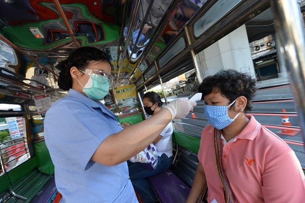 A health worker examines a person's body temperature at a checkpoint in Bangkok, Thailand, on March 26 (Photo: Xinhua/VNA)