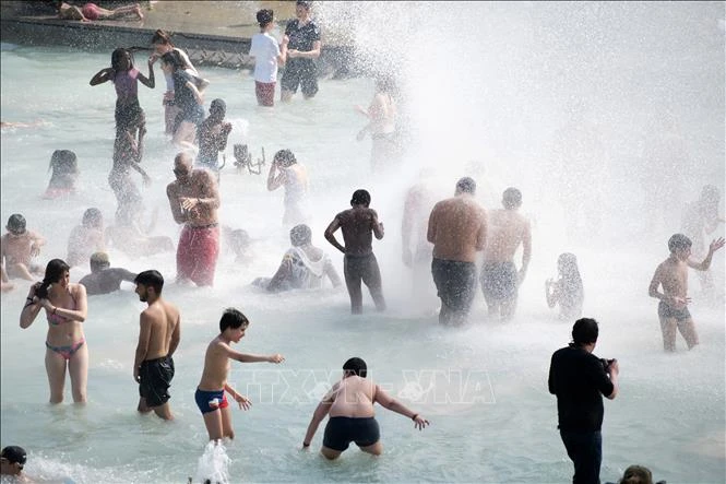 Người dân tránh nắng nóng bên vòi phun nước ở Paris, Pháp, ngày 26/6/2019. Ảnh: THX/TTXVN