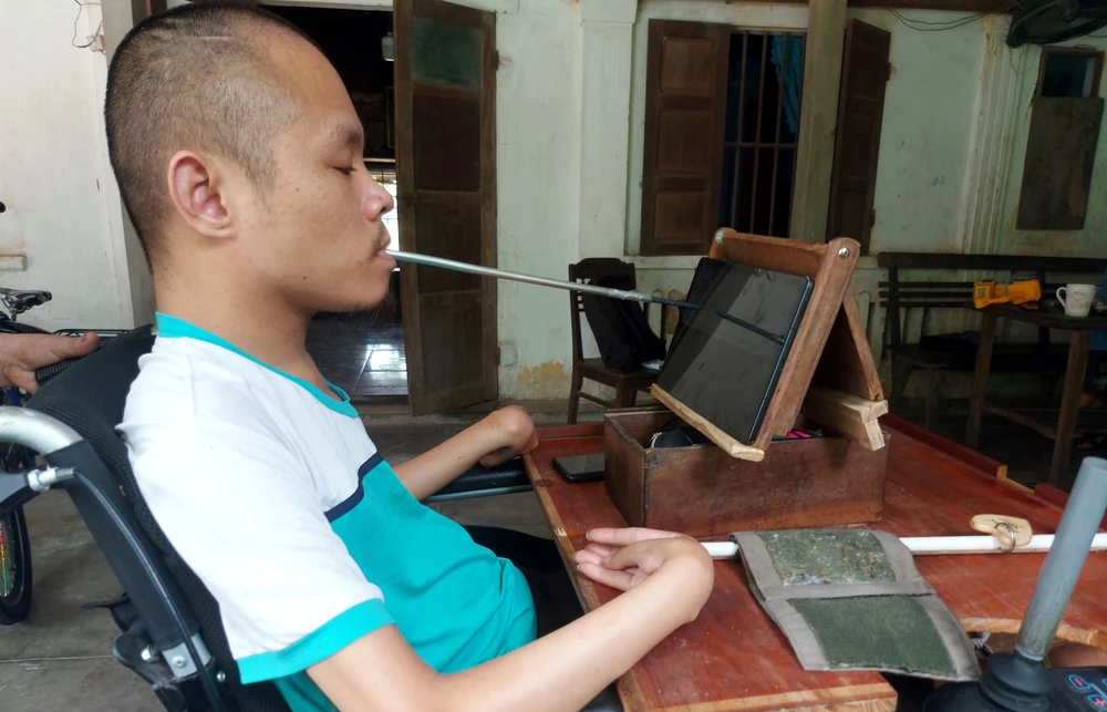 Anh Phạm Sỹ Long ngồi xe lăn ngậm bút tự chế viết truyện trên máy tính bảng