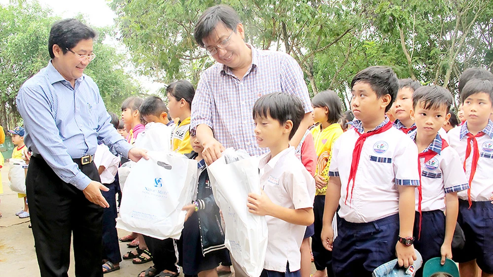 PGS-TS Trần Văn Ngọc (bìa trái) và bác sĩ Cao Xuân Minh tặng quà học sinh Trường Tiểu học Tân Hòa