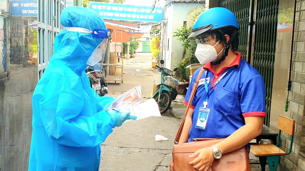 Anh Châu Tiến Lộc (phải), cán bộ Thành đoàn TPHCM, cùng nhân viên y tế nắm tình hình F0 điều trị tại nhà