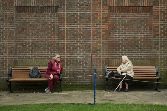 Two women keep 6 feet (1.8 meters) apart as they speak to each other from adjacent park benches amidst the novel coronavirus COVID-19 pandemic, in the centre of York, northern England on March 19, 2020. (Image: © OLI SCARFF/AFP via Getty Images)