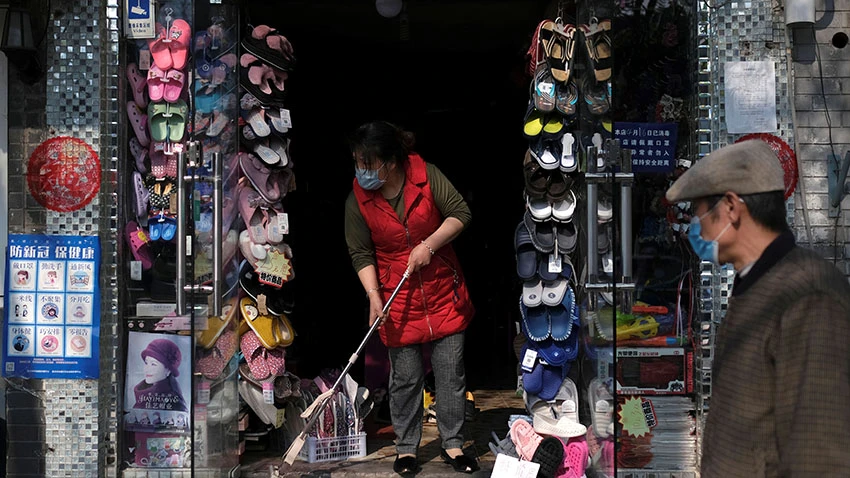 A woman wearing a face mask cleans the entrance of a shop in Beijing on April 17. The coronavirus outbreak has hit China's domestic demand hard. © Reuters