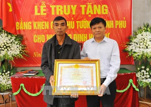 Phó Tổng Giám đốc Thông tấn xã Việt Nam Đinh Đăng Quang thừa ủy quyền của Thủ tướng Chính phủ trao Bằng khen của Thủ tướng Chính phủ cho gia đình cố Nhà báo Đinh Hữu Dư. Ảnh: TTXVN