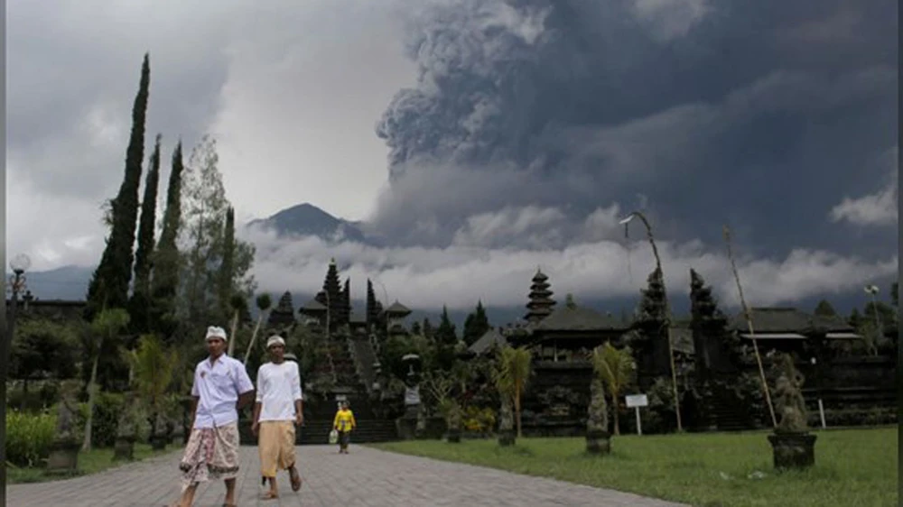 Người dân Bali đi bộ tại đền Besakih ở Karangasem, Bali, Indonesia, phía sau là núi lửa Agung phun trào, ngày 26-11-2017. Ảnh: REUTERS