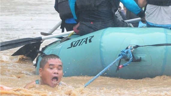 A man clings onto the rope of a rescue boat as residents are evacuated from their homes due to heavy flooding in Cagayan de Oro city in the Philippines CREDIT: FROILAN GALLARDO/REUTERS