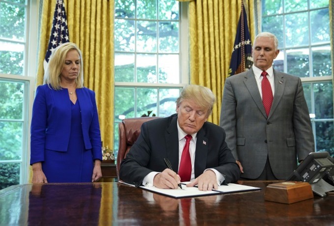 US President Donald Trump -- flanked by Homeland Security Secretary Kirstjen Nielsen (left) and Vice President Mike Pence -- signs an executive order to end family separations at the border.—AFP/VNA Photo
