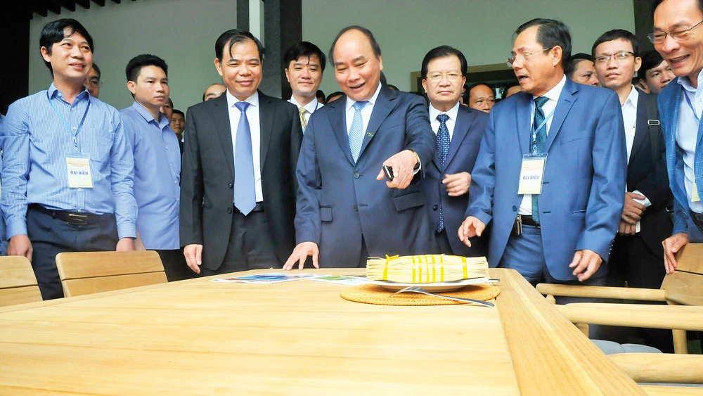 Thủ tướng Nguyễn Xuân Phúc xem sản phẩm đồ gỗ sản xuất trong nước trưng bày tại Hội nghị về định hướng, giải pháp phát triển nhanh, bền vững ngành công nghiệp chế biến gỗ và lâm sản xuất khẩu ngày 8-8. Ảnh: CAO THĂNG