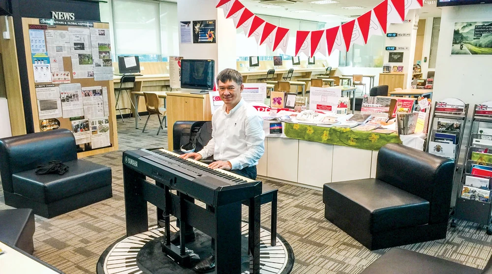 Tác giả và cây đàn dương cầm đặt trong thư viện trường quốc tế.
