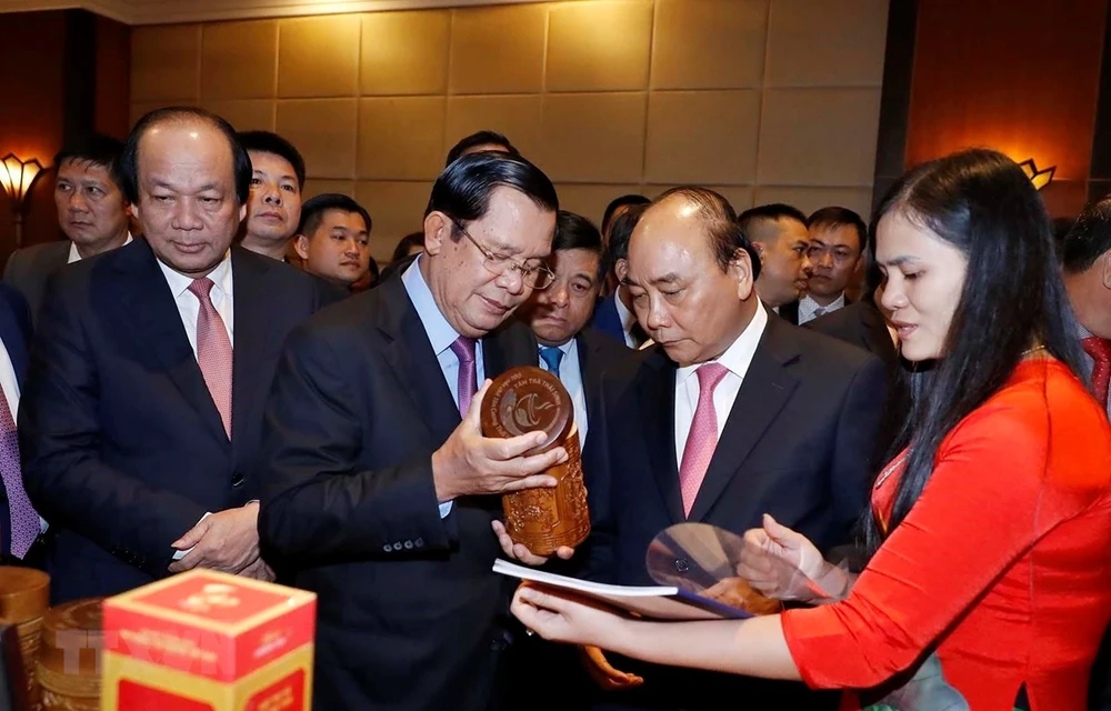 Thủ tướng Nguyễn Xuân Phúc và Thủ tướng Vương quốc Campuchia Samdech Techo Hun Sen xem các sản phẩm của doanh nghiệp trưng bày tại hội nghị. (Ảnh: Thống Nhất/TTXVN)