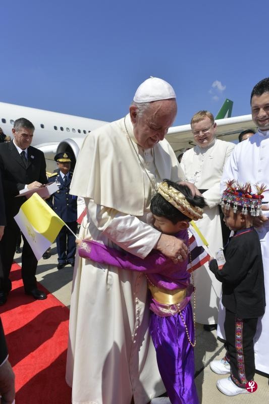 教宗方濟各昨天飛抵曼谷廊曼國際機場時，受到民眾熱烈歡迎，並與一名身穿少數族群傳統服裝的孩童擁抱。 （法新社）