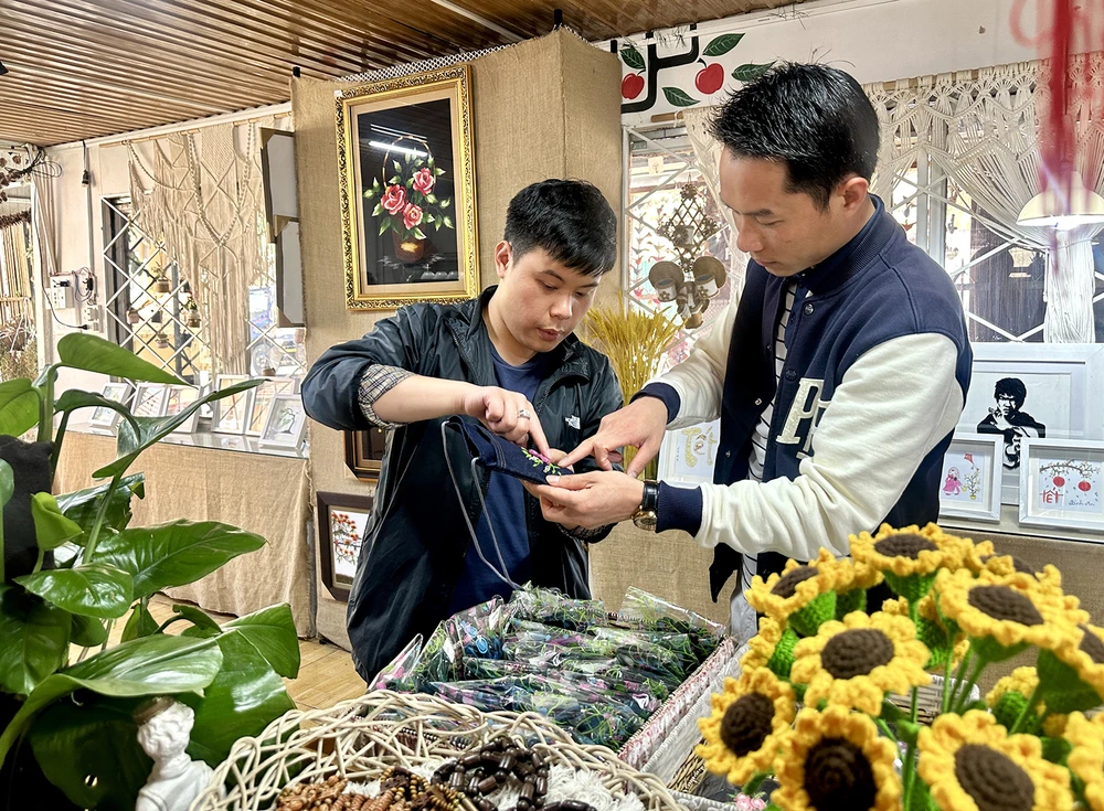 Nguyễn Lưu Quang, học sinh Trường Khiếm thính Lâm Đồng (bên trái), giới thiệu cho khách những sản phẩm do chính các bạn khiếm thính làm ra
