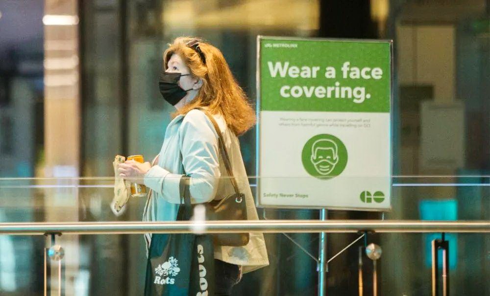 在加拿大多倫多一座車站，一名戴口罩的女子從提醒人們戴口罩的告示旁走過。