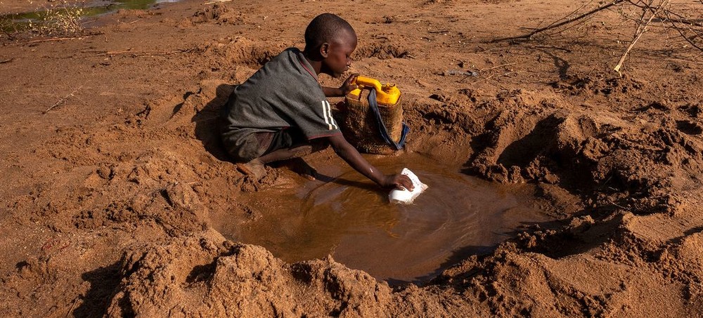 小男孩正從一條乾涸的河流中收集他所能收集到的水。