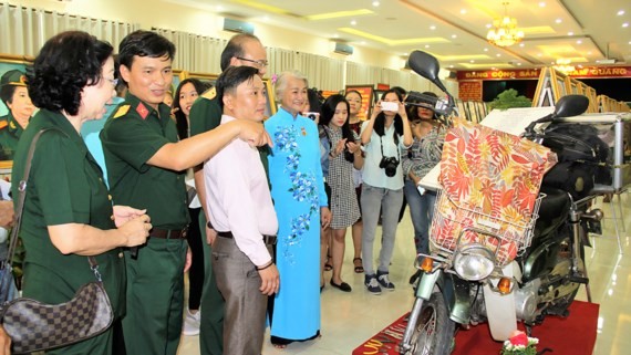 Painter Dang Ai Viet (Blue Ao Dai) presents to visitors her motorbike that she rode it to various parts of the country. (Photo: Sggp)