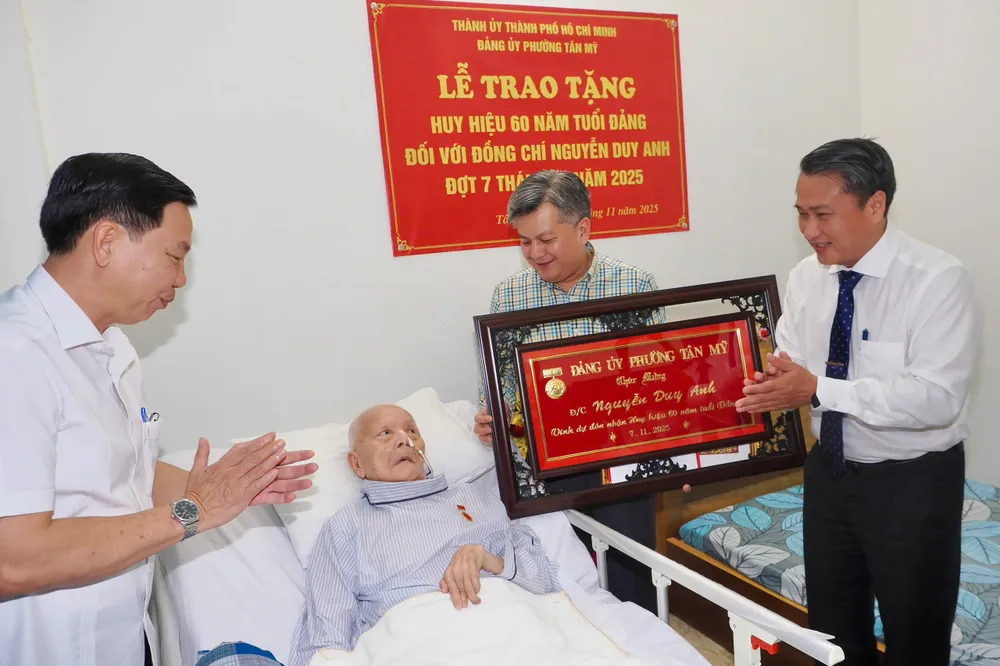 Bí thư Đảng ủy phường Trần Chí Dũng và Phó Bí thư Thường trực Đảng ủy phường Nguyễn Dũng Hùng trao khánh vàng chúc mừng. Ảnh: HOÀNG HÙNG