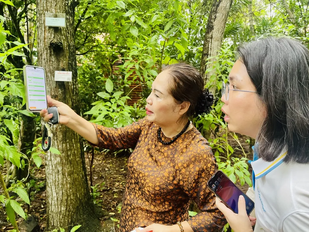 Bà Lê Thị Nga hướng dẫn du khách quét mã QR gắn trên thân cây để đọc chỉ số lưu trữ carbon của từng cây Mrs Nga.jpg
