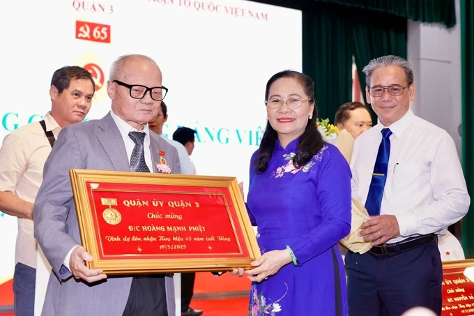 Mrs. Nguyen Thi Le presents the 65-year Party membership badge to veteran Party member of District 3 Hoang Manh Phiet. (Photo: SGGP/ Hoang Hung) hinh-5-6208-2487.jpg