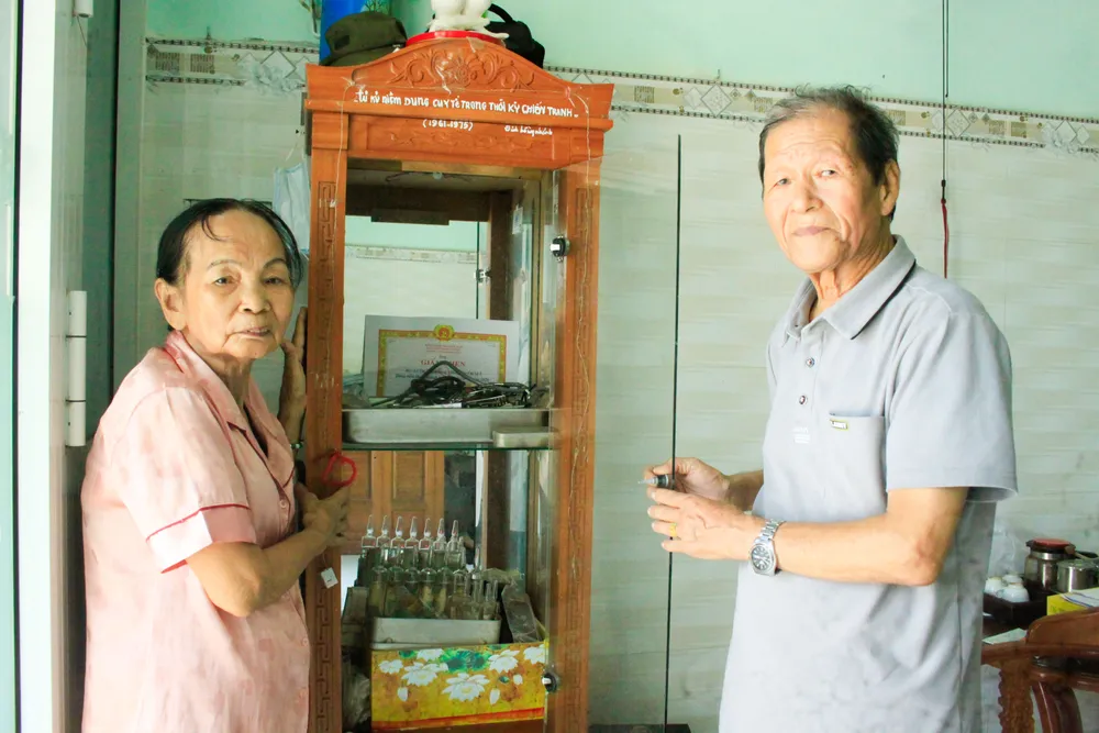 Hai vợ chồng cựu chiến binh Đinh Hồng Khánh (80 tuổi) và bà Lê Thị Thanh Hồng (80 tuổi, phường Cẩm Thành, tỉnh Quảng Ngãi) giữ gìn những kỷ vật trong tủ kính. Ảnh: NGUYỄN TRANG y te 2 láy (1 of 1).jpg