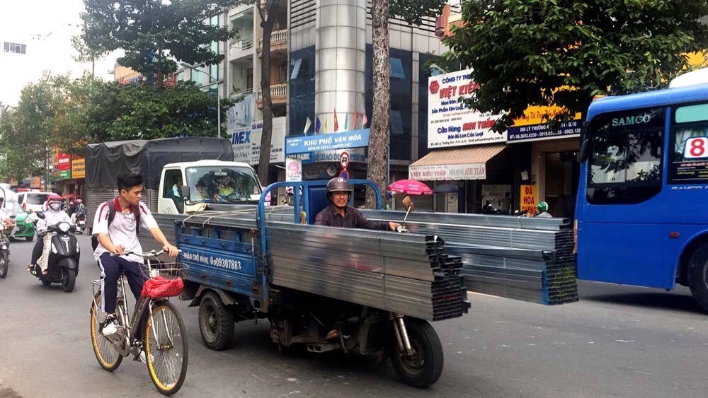 在第十一郡交通密度高的李常傑街上通行的機動三輪車，車上載著特長鐵枝，突出車外的兩頭都沒包住。