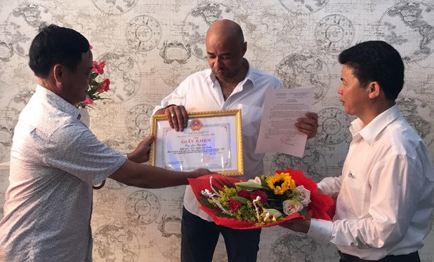 峴港市蓮沼郡郡委書記武功政(右一）和該郡人委會副主席阮友鐵(左一)向法籍遊客讓‧克里斯托夫頒贈獎狀並送鮮花。（圖源：阮秀）