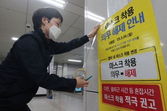 当地时间2023年3月19日,韩国首尔,在首尔地铁站,相关人士正在贴告示。从3月20日起,在公共交通工具上戴口罩的义务将被取消。(图:互联网)