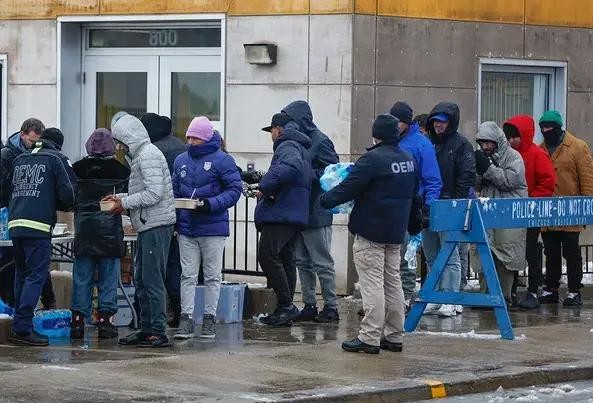 1月12日,芝加哥冬季暴风雨期间,一群移民在移民登陆区外领取食物。(图:路透社)