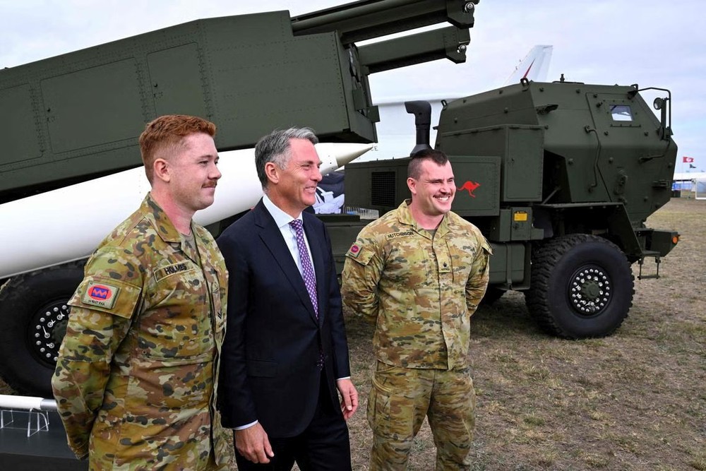 澳洲国防部长马尔斯（中）3月24日出席澳洲国际航展，他与两名士兵在一辆高机动炮兵火箭系统（HIMARS）旁拍照。（图：AFP）