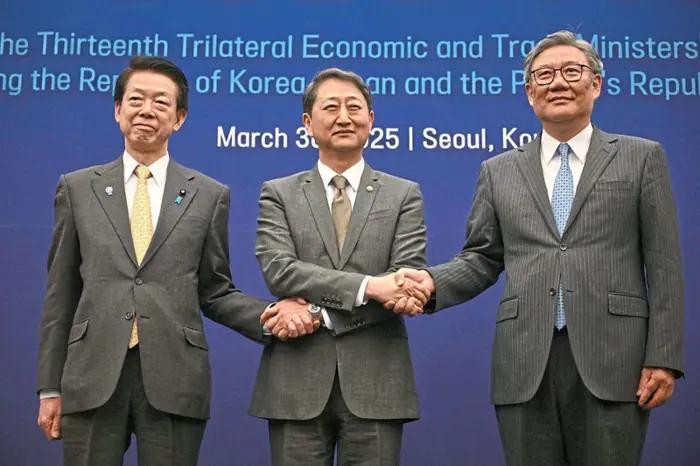 图为日本经济产业大臣武藤容治（左起）、韩国产业通商资源部长官安德根、中国商务部部长王文涛握手合影。（图：AFP）