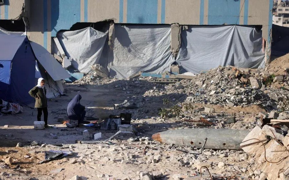 4月19日，加沙地带加沙城一个由警察局改建的避难所附近，一名流离失所的巴勒斯坦妇女和另一名妇女在未爆炸弹药附近的帐篷前。（图：AFP）