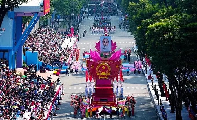 越南社会主义共和国国徽模型车引领阅兵游行方队。紧随其后的是载着胡志明主席肖像的车辆在本市中心行驶，两侧是数千人民挥手欢迎。