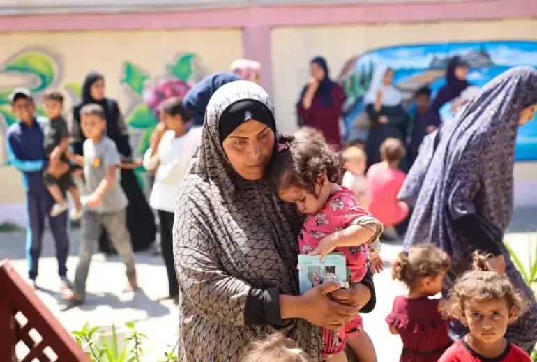  在加沙地带由联合国儿童基金会支持的一家诊所，一名妇女抱着她的女儿等待接受营养筛查。（图：UNICEF）