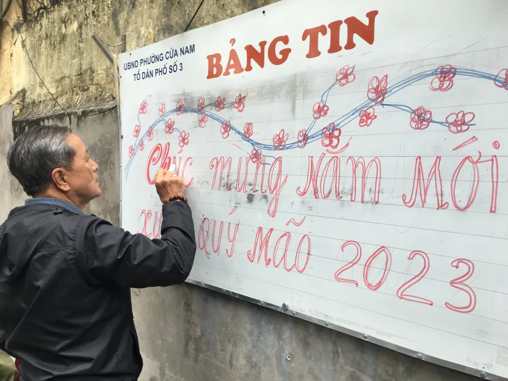 Tổ trưởng một tổ dân phố ở phường Cửa Nam (Hà Nội) nắn nót viết dòng chữ chúc mừng năm mới. Ảnh: VĂN PHÚC