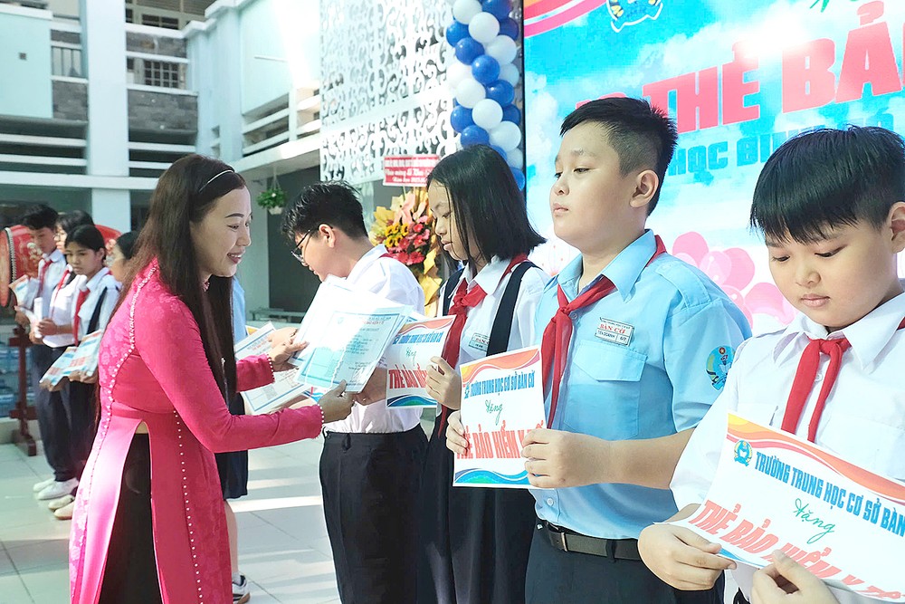 棋盘初中学校校长阮氏清泉在新学年开学典礼上向学生赠送医保卡。 