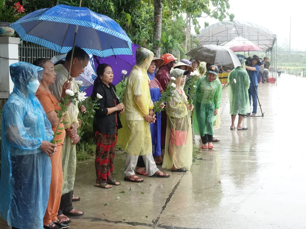 Người dân đội mưa, cầm bông hoa cúc trắng đứng đón linh cữu liệt sĩ Lê Ánh Sáng Người dân đội mưa, cầm bông hoa cúc trắng đứng đón linh cữu liệt sĩ Lê Ánh Sáng