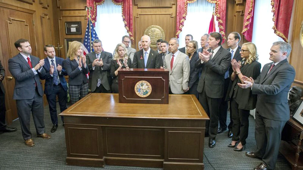 Thống đốc Rick Scott ký ban hành luật hạn chế súng tại Văn phòng Thống đốc ở Tallahassee, Florida, Mỹ, ngày 9-3-2018, dưới sự chứng kiến của các thành viên gia đình nạn nhân vụ xả súng trường học ở Parkland, Florida, Mỹ, ngày 14-2-2018. Ảnh: AP