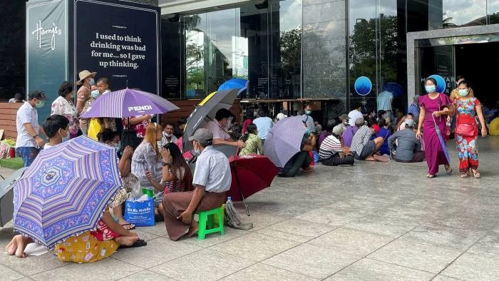 Người dân Yangon mang theo ghế đẩu và ô để khiến việc chờ đợi lâu bên ngoài các ngân hàng dễ chịu hơn. © Reuters