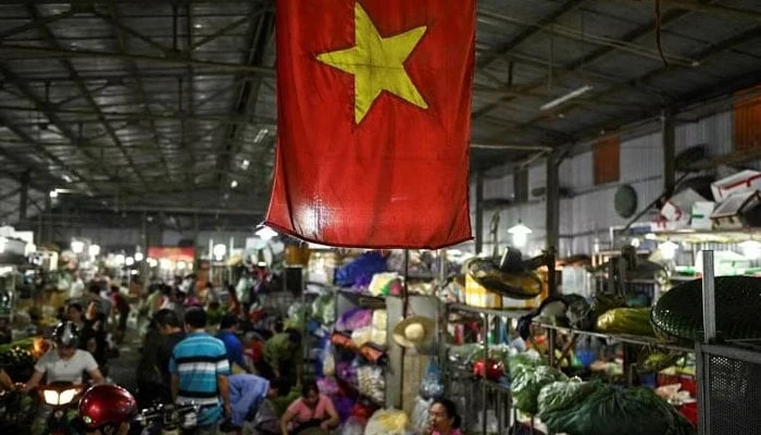 The Vietnamese flag is seen as vegetable vendors wait for customers at a wholesale market in Hanoi, Vietnam. — AFP 