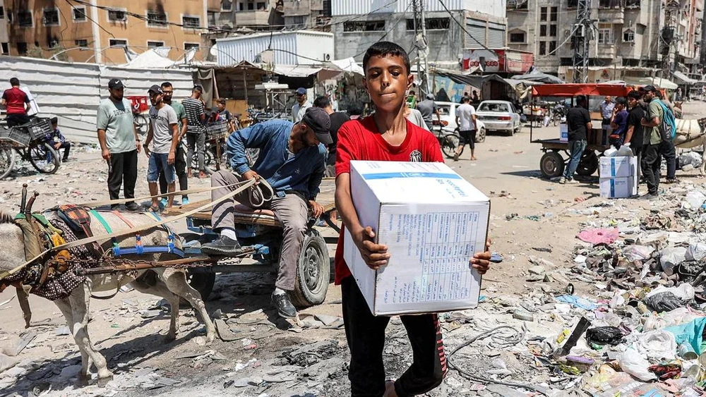 Một cậu bé mang gói hàng viện trợ nhân đạo do UNRWA cung cấp tại trung tâm thành phố Gaza vào ngày 27/8. @Omar Al-Qattaa/AFP/Hình ảnh Getty