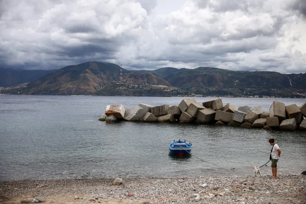 Một người phụ nữ dắt chó đi dạo dọc bờ biển Sicily, bên kia eo biển Messina, Ý, ngày 5 tháng 8 năm 2025. Khu vực này là một phần của địa điểm dự kiến xây dựng cây cầu treo nối Sicily với đất liền Ý, dự kiến khởi công xây dựng vào nửa cuối năm 2025. Ảnh: Yara Nardi