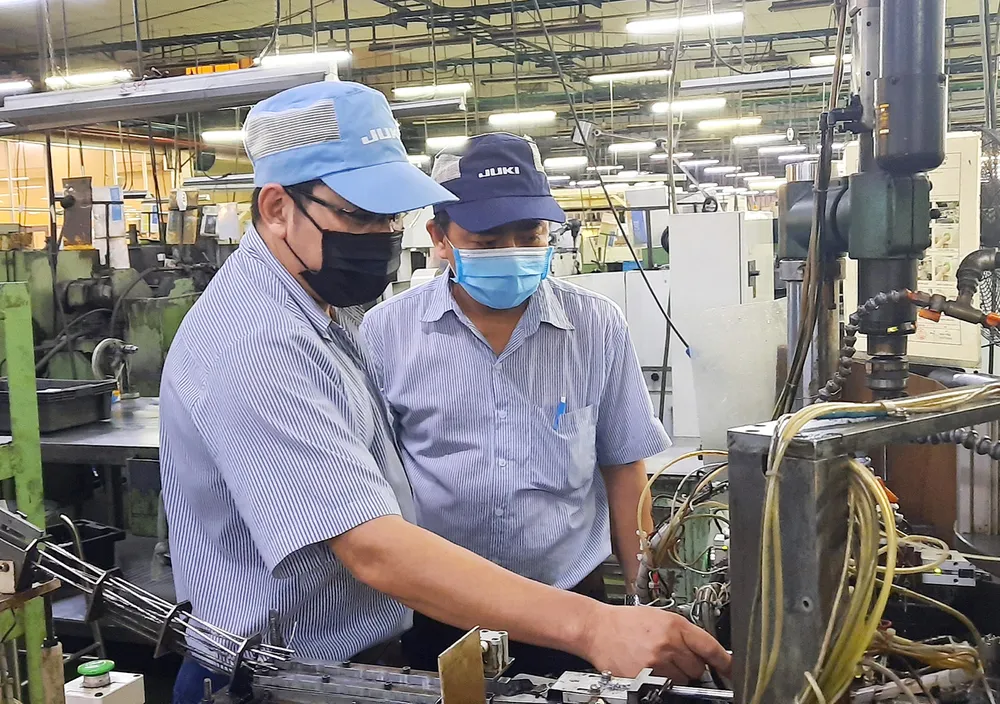 Anh Lê Chí Chung (trái, Công ty Juki) cùng đồng nghiêp tìm hiểu hoạt động của máy để đưa ra sáng kiến cải tiến. Ảnh: THÁI PHƯƠNG