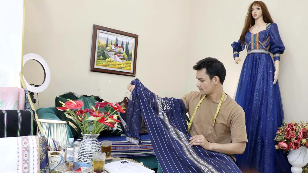 Anh K’Jona bên sản phẩm thổ cẩm kết hợp chất liệu ren do mình thiết kế Anh K’Jona bên sản phẩm thổ cẩm kết hợp chất liệu ren do mình thiết kế