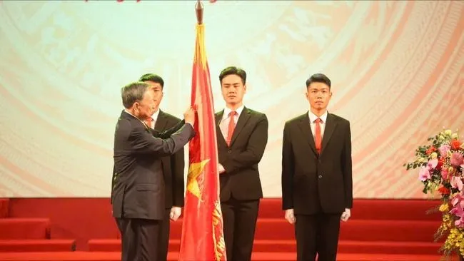 Tổng Bí thư Tô Lâm gắn Huân chương Lao động hạng Nhất lên lá cờ truyền thống. Ảnh: VIẾT CHUNG