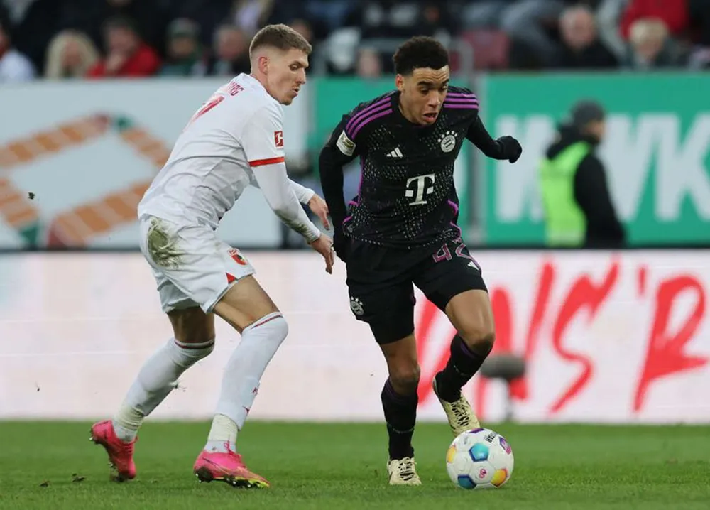 Jamal Musiala (phải, Bayern Munich) đi bóng qua hậu vệ Kristijan Jakic (Augsburg)