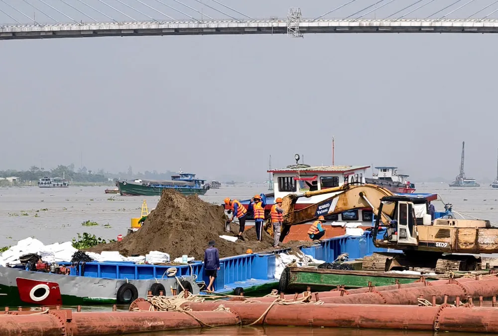 Công nhân được trang bị áo phao thực hiện công đoạn đóng bao tải gia cố mái lòng sông trên sà lan.