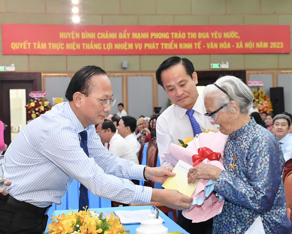 Bí thư Huyện ủy huyện Bình Chánh Trần Văn Nam và Chủ tịch HĐND huyện Bình Chánh Phạm Văn Lũy tặng hoa tri ân Mẹ Việt Nam Anh hùng. Ảnh: VIỆT DŨNG